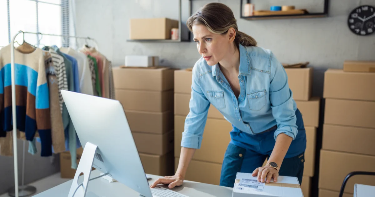 Clothing founder working at a studio desk beside a garment rail